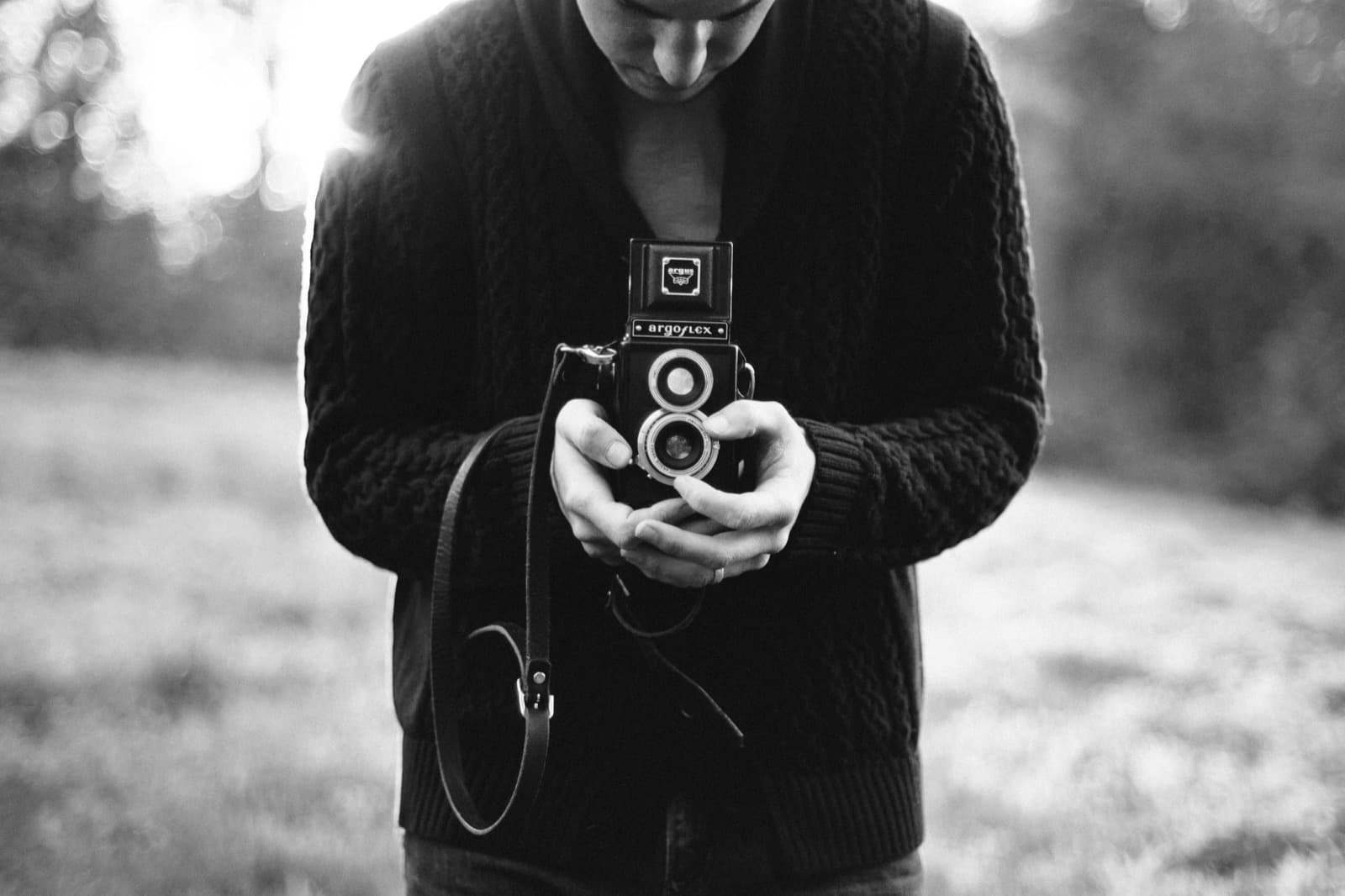 A photographer looking down into a twin-lens camera, black and white photograph